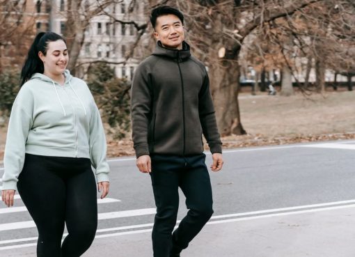 Positive young multiethnic male and female friends in sportswear smiling while crossing asphalt road near city park after outdoor training
